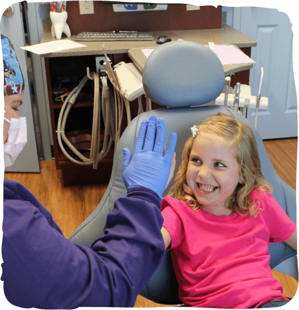 Young girl smiling during dental examination in pediatric dentist office with equipment visible.