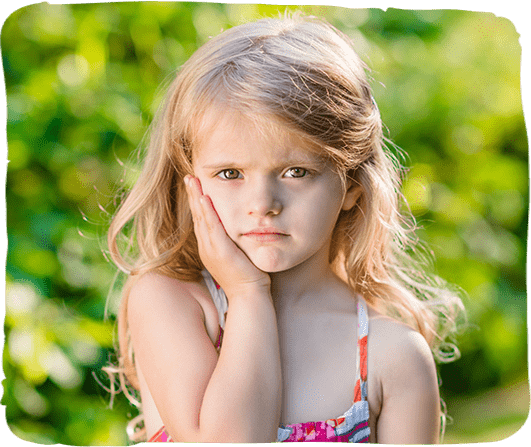 Young girl with blonde hair looking thoughtful outdoors in green garden setting.
