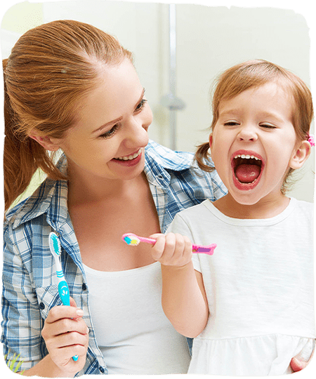 Mother and young child brushing teeth together in bathroom, smiling during dental care routine.