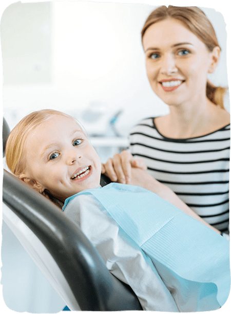Mother and smiling toddler in dental chair during pediatric dental appointment.