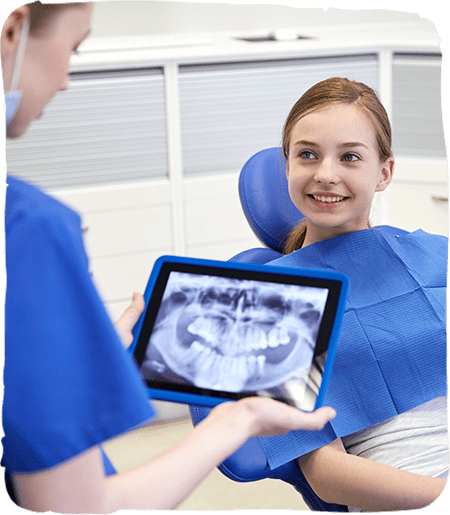 Pediatric dentist showing young patient digital X-ray on tablet in modern dental office.