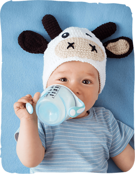 Baby wearing cow hat drinks from bottle on blue background.