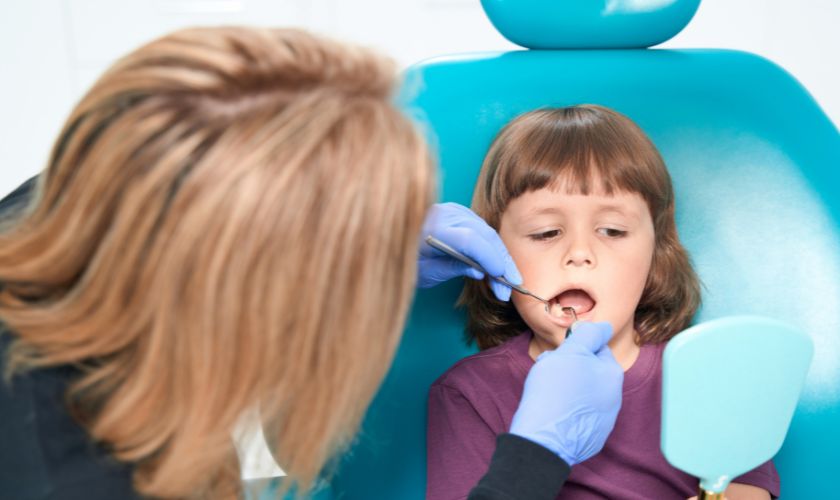 Pediatric dentist examining young child's teeth during dental checkup in clinical setting.