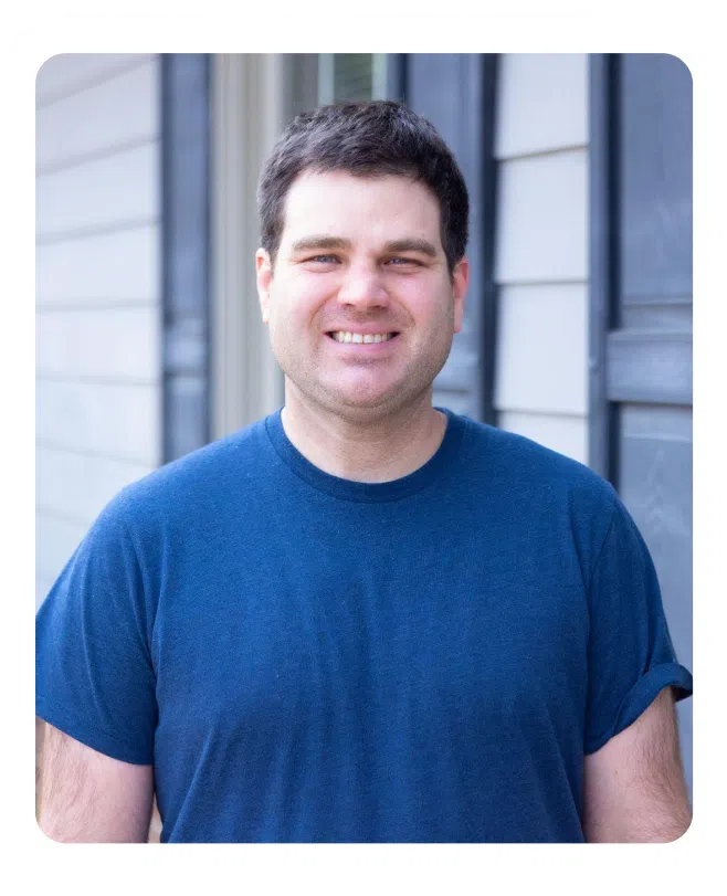 Smiling man in blue shirt against blurred indoor background for pediatric dentistry website.