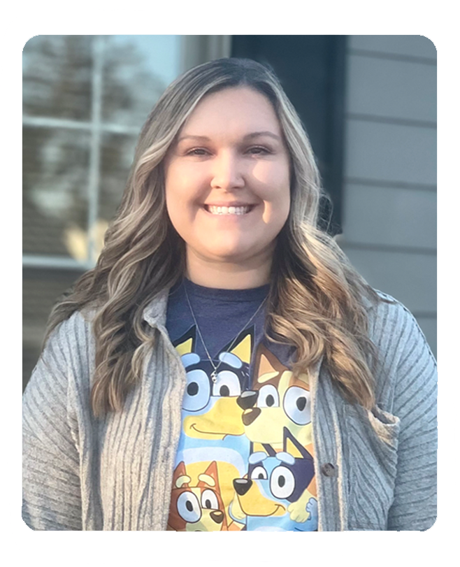 Smiling woman wearing Bluey character shirt standing outdoors in front of building.