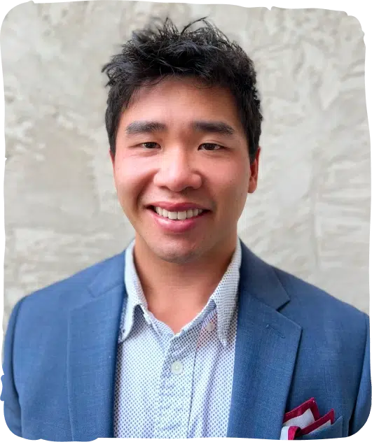 Smiling male pediatric dentist in blue blazer and light blue shirt against neutral background.